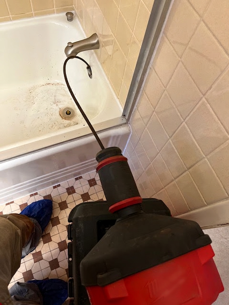 BF Plumbing technician using a drum auger to clear a clogged bathtub drain