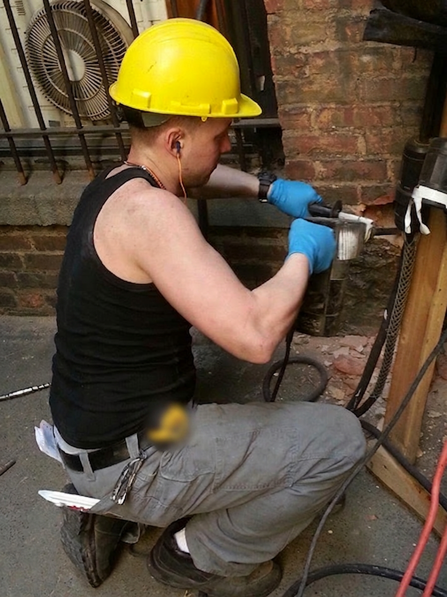 Plumber in safety gear demolishing brick to reach a burst pipe behind a wall