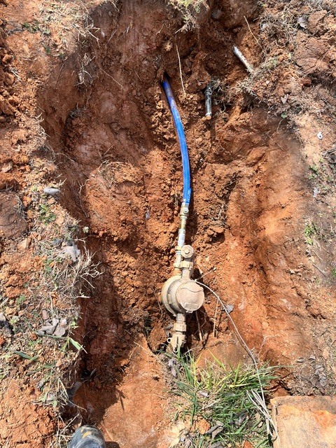 Exposed water service line and pressure-reducing valve in an open trench during an underground leak investigation