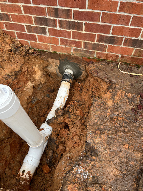 Close-up of a freshly tied-in PVC sewer cleanout at the brick foundation after a sewer line repair