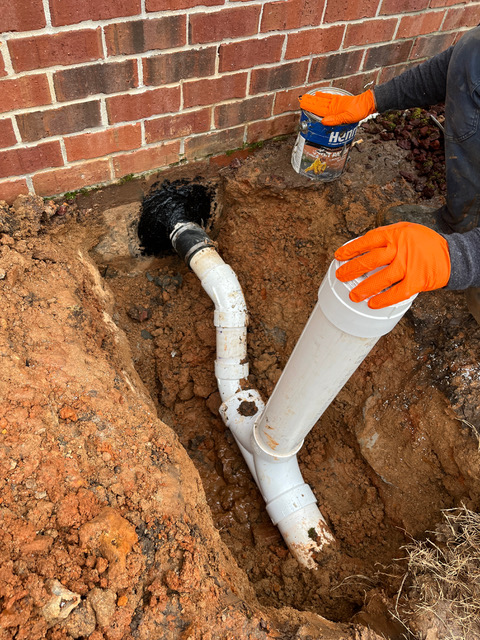 BF Plumbing technician dry-fitting a new PVC cleanout into a replaced sewer line at the foundation
