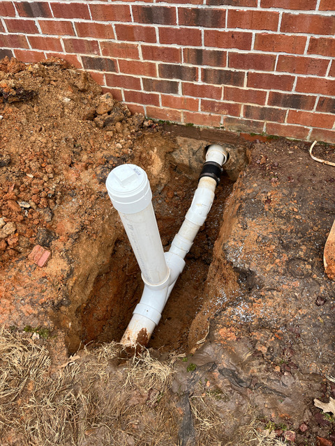 New PVC sewer cleanout riser installed at the foundation of a brick home